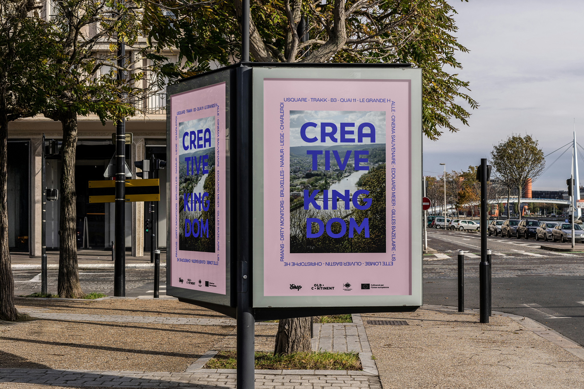 Two Creative Kingdom event posters displayed on a street advertising panel, featuring bold blue typography on a pink background with an aerial landscape photograph and a list of participating artists and cities.