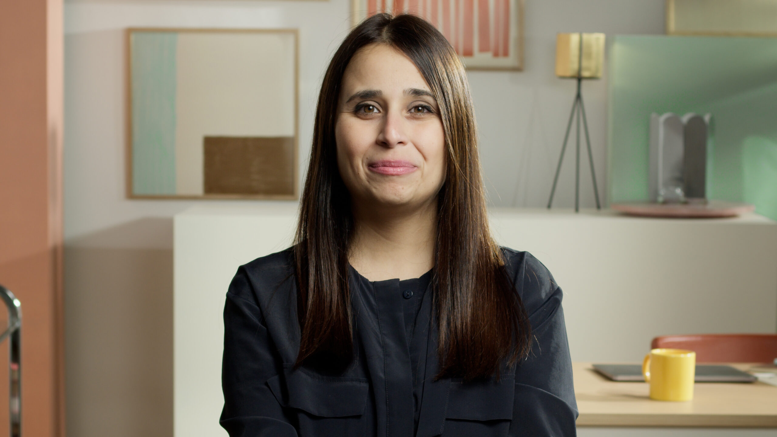 A researcher being interviewed on camera, seated in front of a carefully designed studio set with colorful abstract artworks on the wall.